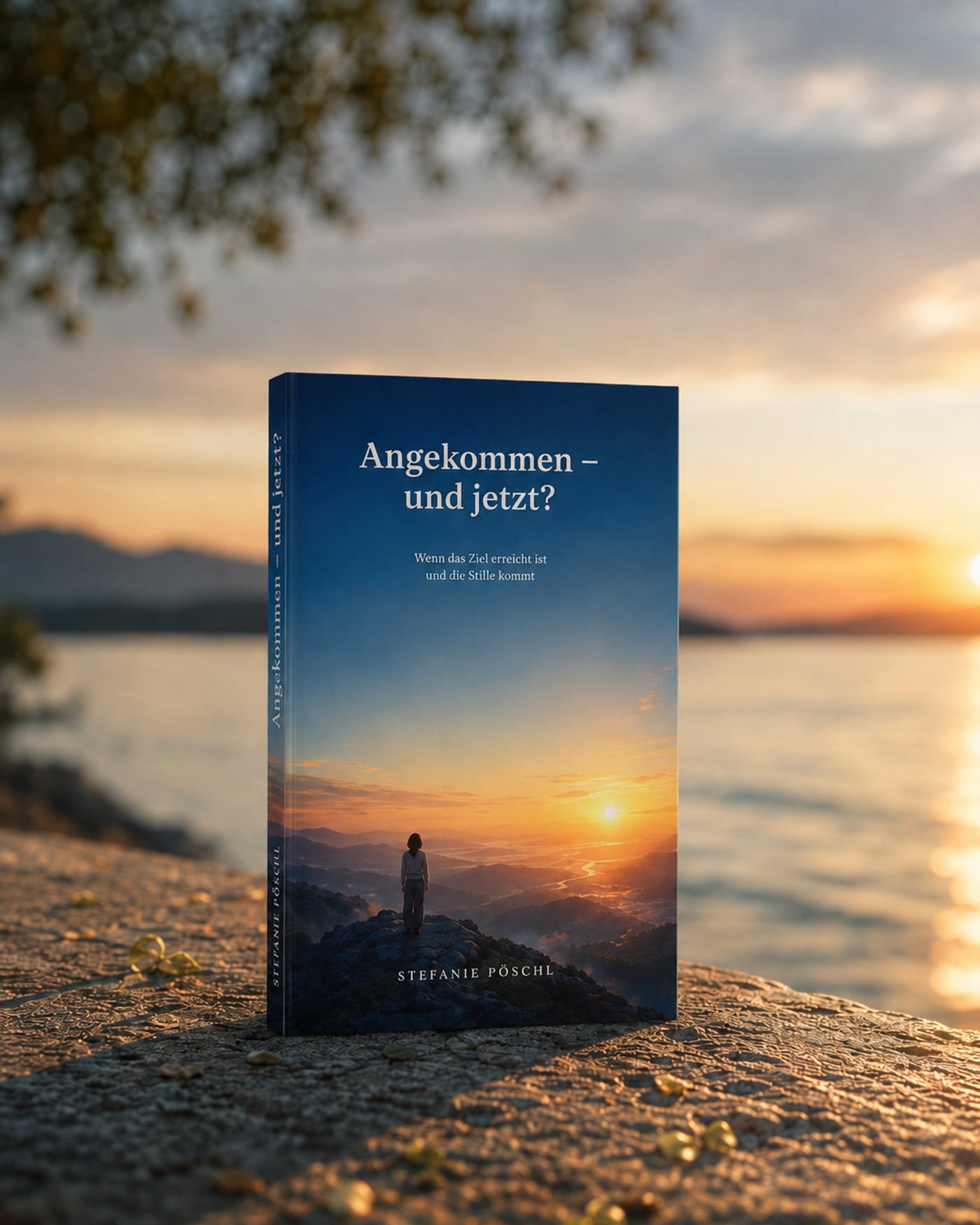 Das Buch „Angekommen — und jetzt?“ steht auf einer Steinmauer am Meer im Sonnenuntergang